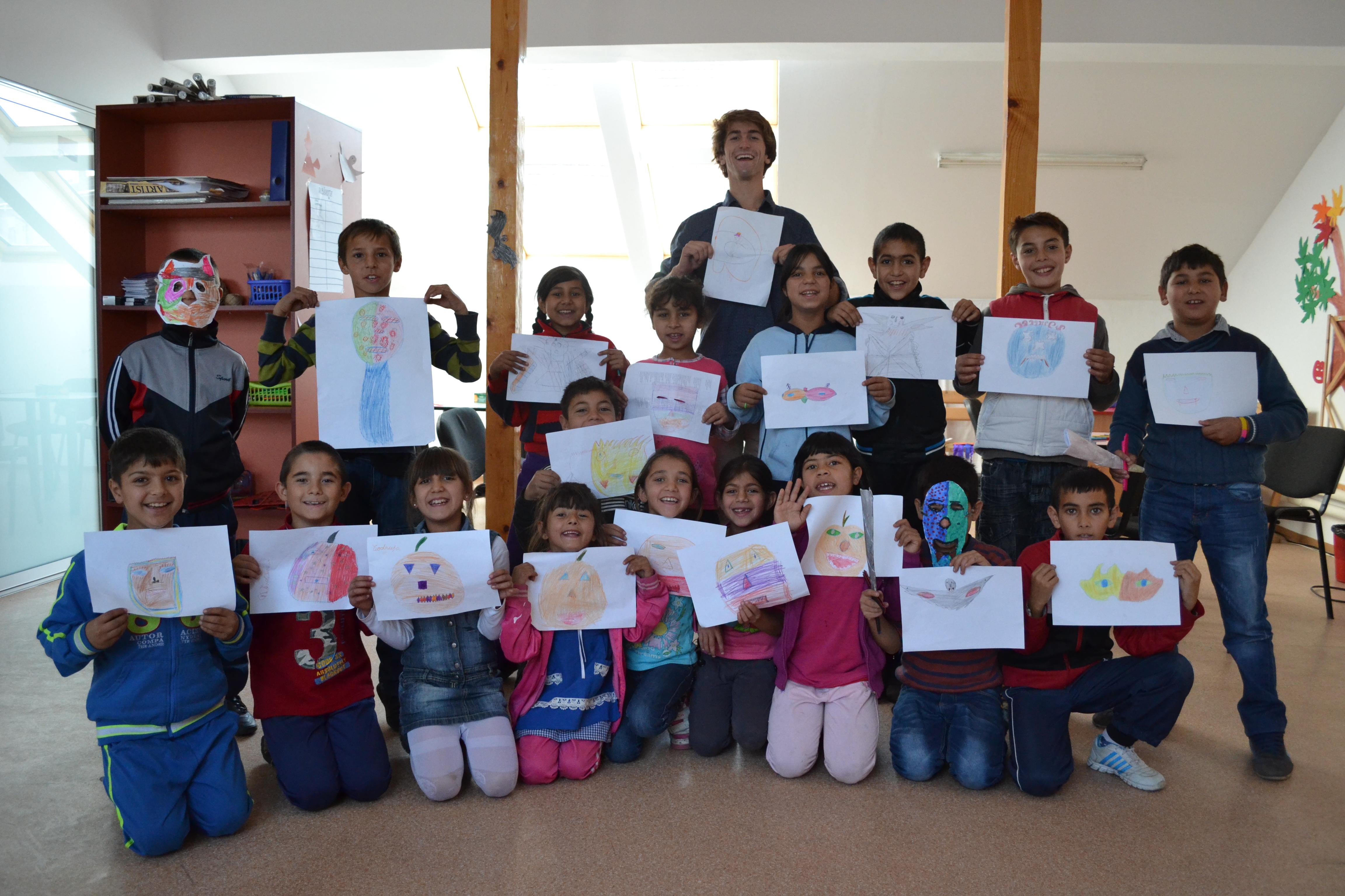 A male volunteer working with children in Romania with the children showcasing their drawings at a care centre. Projects Abroad male volunteer with children holding their drawings at a Childcare placement in Romania.